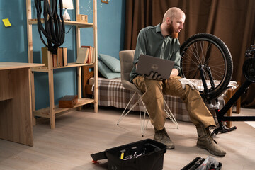 Bearded cyclist searching bike components repair cycling using laptop. Man reading instructions to...