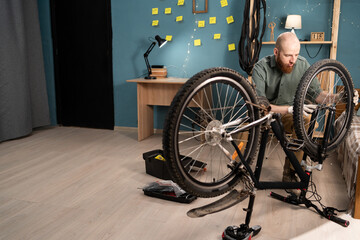 Bearded man in casual clothes servicing repairing bicycle at home. Hobby and DIY