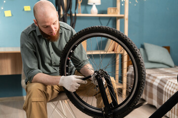 Bearded man in casual clothes servicing repairing bicycle at home. Hobby and DIY