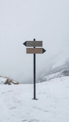 Naklejka premium A minimalist photograph of a black metal directional signpost in a snow-covered landscape
