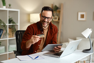 Happy freelancer paying online with credit card and digital tablet at home