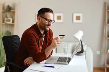Freelancer smiling and making online payment with credit card at home