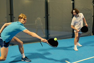 Exciting moments of young sportsmen playing padel on a vibrant indoor court