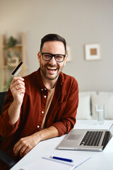 Happy entrepreneur showing credit card while working remotely from home