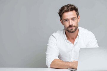 Young caucasian man wearing a white shirt sitting on a desk using laptop computer isolated over light grey background. Business concept.