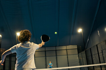 Young sportsmen engage in an exciting padel match on a vibrant court in the evening