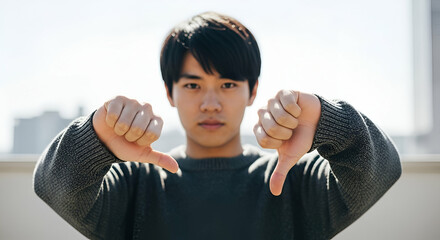 Young man expressing disapproval with thumbs down gesture outdoors against a clear sky backdrop, showcasing a moment of dissatisfaction or frustration