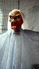 Halloween monster with glowing eyes screaming and hanging from the ceiling, covered by a white...