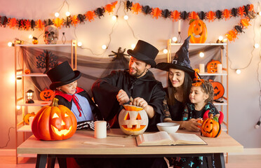 Happy family curving pumpkin for Halloween, wearing festive costumes and preparing for holiday...