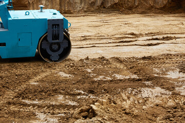 Construction site features a blue roller compacting earth on a freshly excavated ground during...