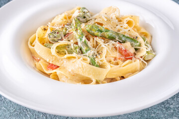 Tagliatelle pasta with creamy garlic sauce, asparagus, peppers, and parmesan topping