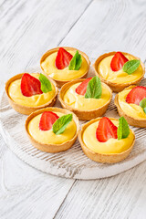 Mini mango cream tarts with strawberry and mint on white wooden board