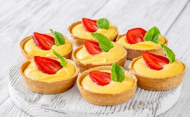 Mini mango cream tarts with strawberry and mint on white wooden board
