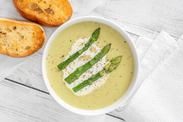 Creamy asparagus soup in white bowl with swirl and toasted ciabatta