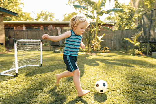 Little boy playing soccer in sunlit backyard