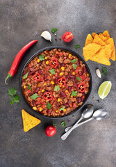 Chili con carne with fresh herbs and nachos chips on a gray background. Top view. Mexican cuisine.
