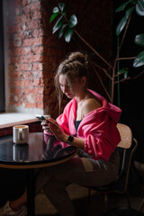 Charming woman with beautiful smile reading good news on mobile phone during rest in coffee shop, happy Caucasian female watching her photo on cell telephone while relaxing in cafe during free time 