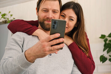 Old couple using a phone together while relaxing in the kitchen at home. Elderly man and woman...