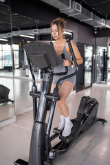 A woman is actively exercising on an elliptical machine at a modern gym facility