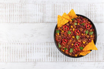 Mexican food chili con carne with beef, beans, corn and chili peppers on white wooden background. Top view. Copy space.