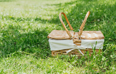 Wicker picnic basket standing alone on green grass in orchard for concepts of rural lifestyle,...