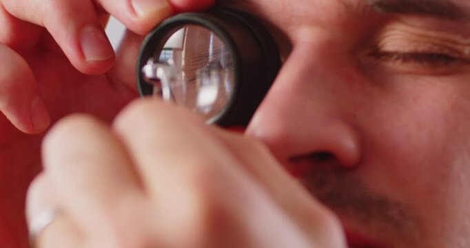 Closeup portrait of male jewellery appraiser inspecting gold ring with diamond looking through magnifying glass isolated on white background. Man jeweler and goldsmith evaluating jewelry. 4k video.