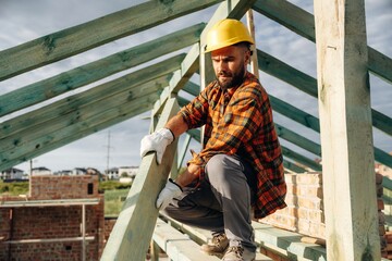 Unfinished place, under sunlight. Construction worker is on the roof of a house