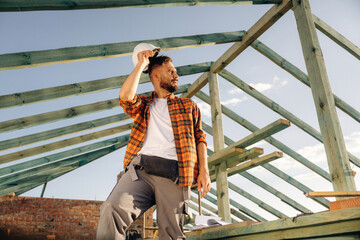 Tired, taking a break. Construction worker is on the roof of a house