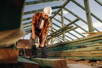 Drilling the holes in plank. Construction worker is on the roof of a house