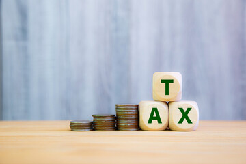 Stacked coins next to wooden blocks spelling "TAX," symbolizing the concept of taxation, savings, and financial planning. Ideal for illustrating topics related to income tax, government revenue,