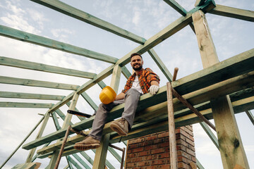 Friendly man is sitting and taking a break. Construction worker is on the roof of a house