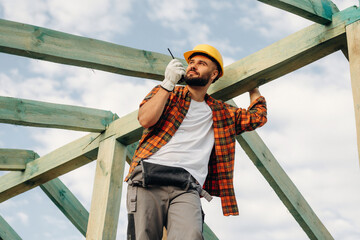 Giving orders by using walkie talkie. Construction worker is on the roof of a house