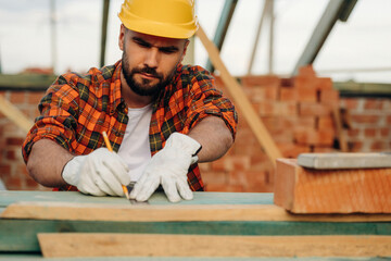 Measuring the length of plank. Construction worker is on the roof of a house