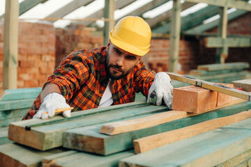 Measuring the length of plank. Construction worker is on the roof of a house