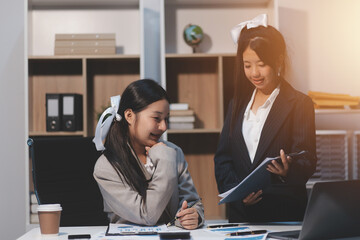 Two young Asian business woman talk, consult, discuss working with new startup project idea presentation analyze plan marketing and investment in the office.