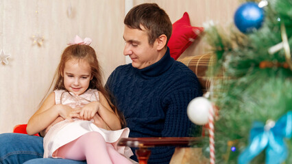 Happy family having fun at home for Christmas. Father tickles her daughter lying on the sofa....