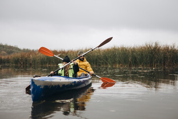 A daughter and her father are paddling in a small canoe in the middle of the lake, holding the oars.