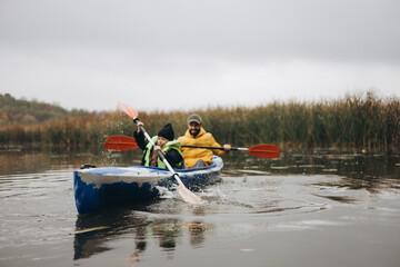 A daughter and her father are paddling in a small canoe in the middle of the lake, holding the oars.