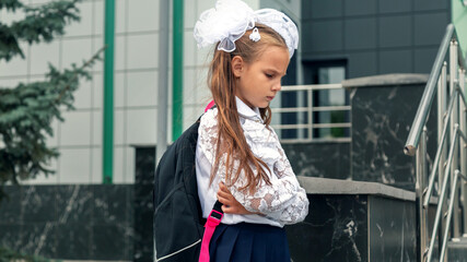 Schoolgirl sadness standing against modern school. Long-haired girl feels bullied by classmates at school