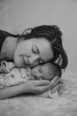A mother peacefully sleeping beside her newborn baby on a soft, textured blanket. The baby is dressed in a cozy outfit, and the scene conveys warmth and tenderness.