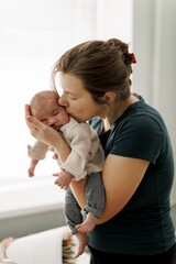 A tender moment between a mother and her newborn baby, with the mother gently kissing the baby's forehead. The baby is wrapped in a soft beige blanket, and the scene conveys warmth and love.