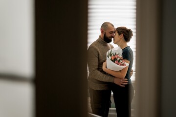 A couple stands close together in a hospital room, gazing at each other with joy. A newborn baby is in a crib nearby, creating a warm and intimate atmosphere.