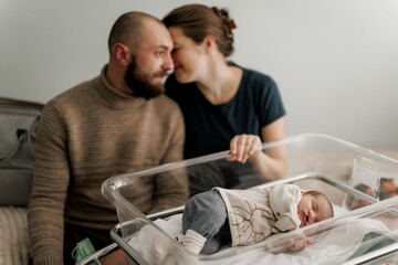 A couple lovingly embraces near a newborn baby in a hospital room.