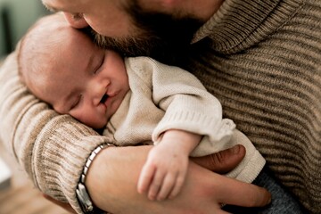 A tender moment between a father and his newborn baby, both lying on a soft surface. The father is gently kissing the baby's forehead, showcasing love and affection.