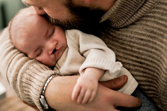 A tender moment between a father and his newborn baby, both lying on a soft surface. The father is gently kissing the baby's forehead, showcasing love and affection.