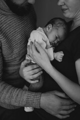 A couple lovingly holds their newborn baby in a cozy indoor setting. The mother gazes at the baby while the father supports them, showcasing a moment of tenderness and family bonding.