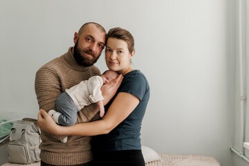A couple lovingly holds their newborn baby in a cozy indoor setting. The mother gazes at the baby...