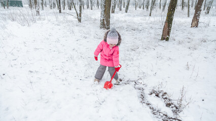 Little girl in colorful clothes play outdoors during a snowfall.