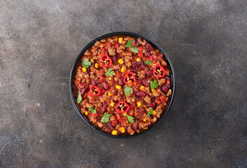 Chili con carne with fresh herbs and nachos chips on a gray background. Top view. Mexican cuisine.