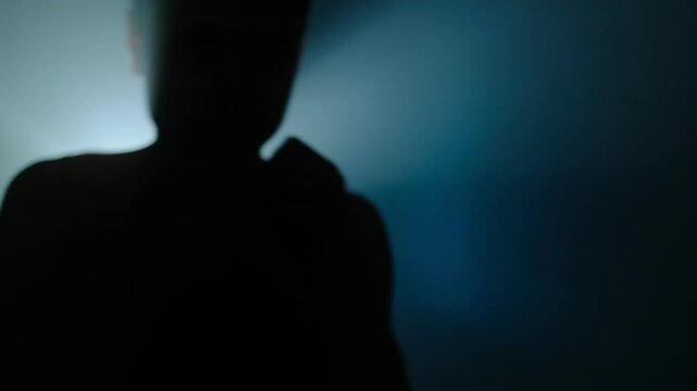 Beginner fighter training punches in silhouette, young man practicing boxing moves in cinematic blue light. Slow motion
